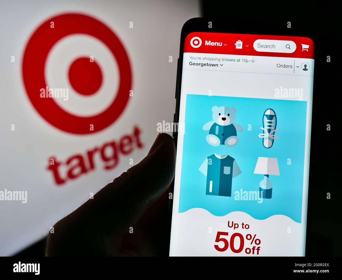 Person holding cellphone with web page of American retail company Target Corporation on screen in front of logo. Focus on center of phone display. Stock Photo