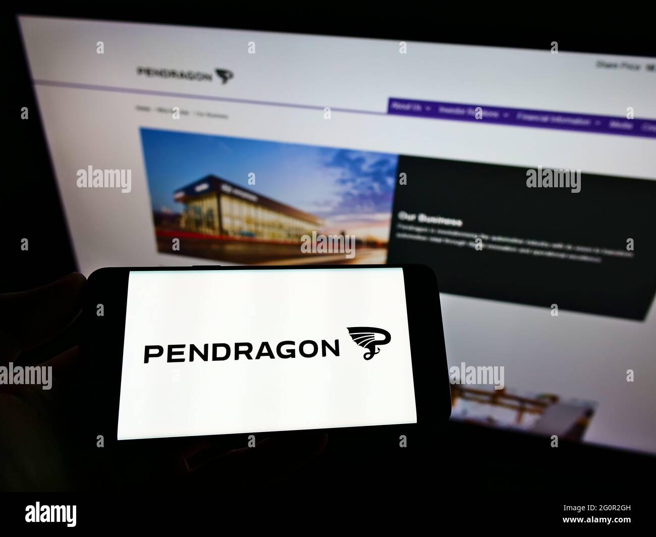 Person holding mobile phone with logo of British automotive retail company Pendragon PLC on screen in front of web page. Focus on phone display. Stock Photo
