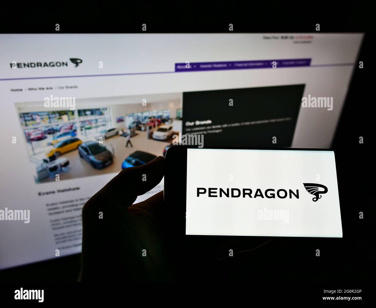 Person holding cellphone with logo of British automotive retail company Pendragon PLC on screen in front of business website. Focus on phone display. Stock Photo