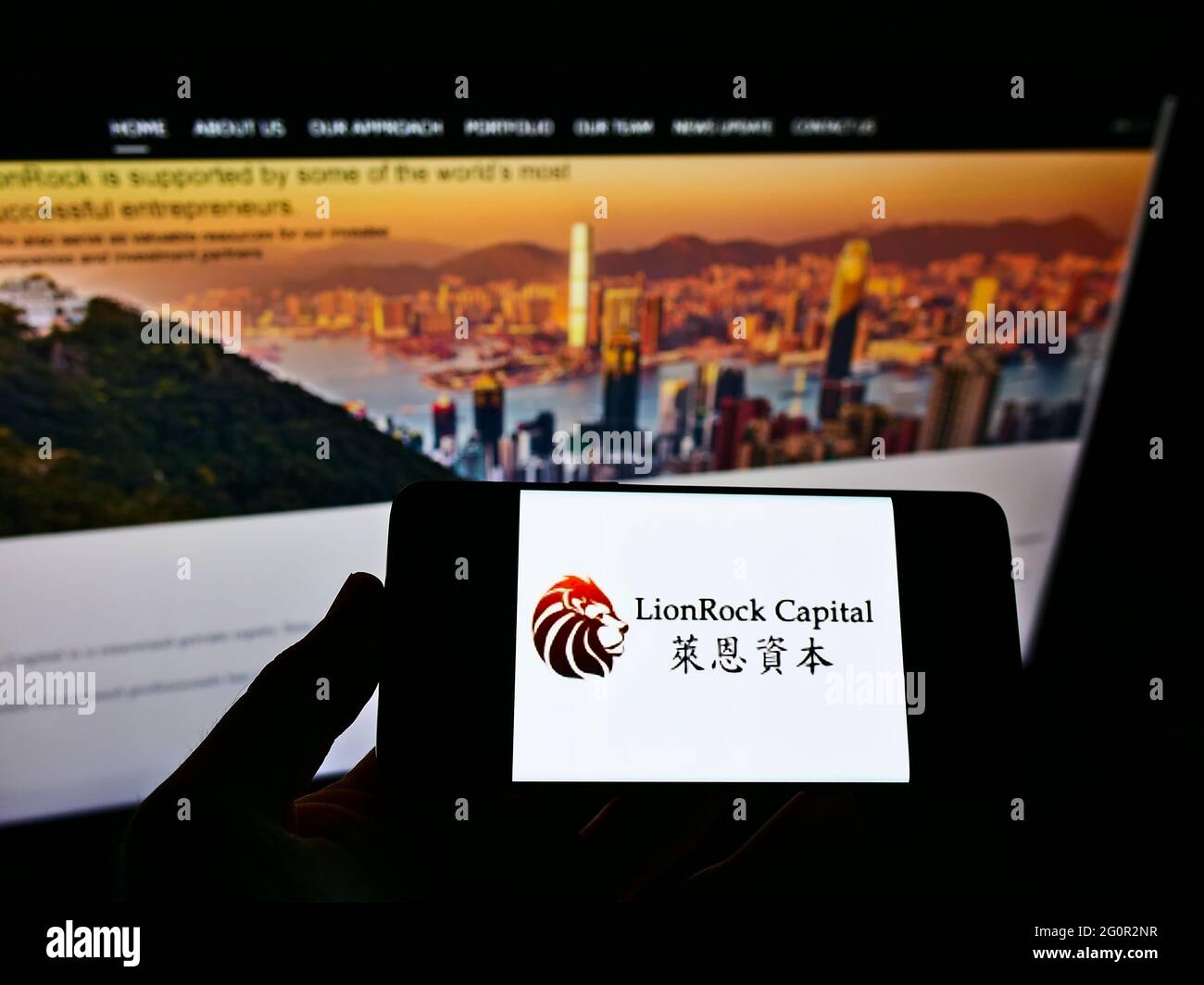 Person holding smartphone with logo of private equity firm LionRock Capital Limited on screen in front of website. Focus on phone display. Stock Photo