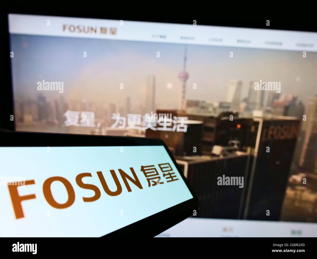 Mobile phone with logo of Chinese conglomerate Fosun International Limited on screen in front of web page. Focus on center-right of phone display. Stock Photo