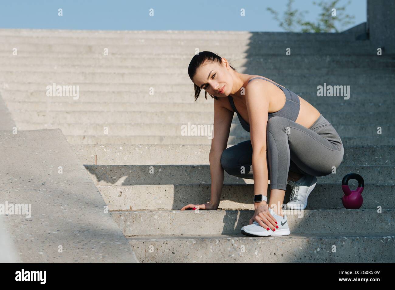 Athletic brunette stretching on the long stairs outdoors, looking at the  camera. In grey top and yoga pants. On a sunny day Stock Photo - Alamy