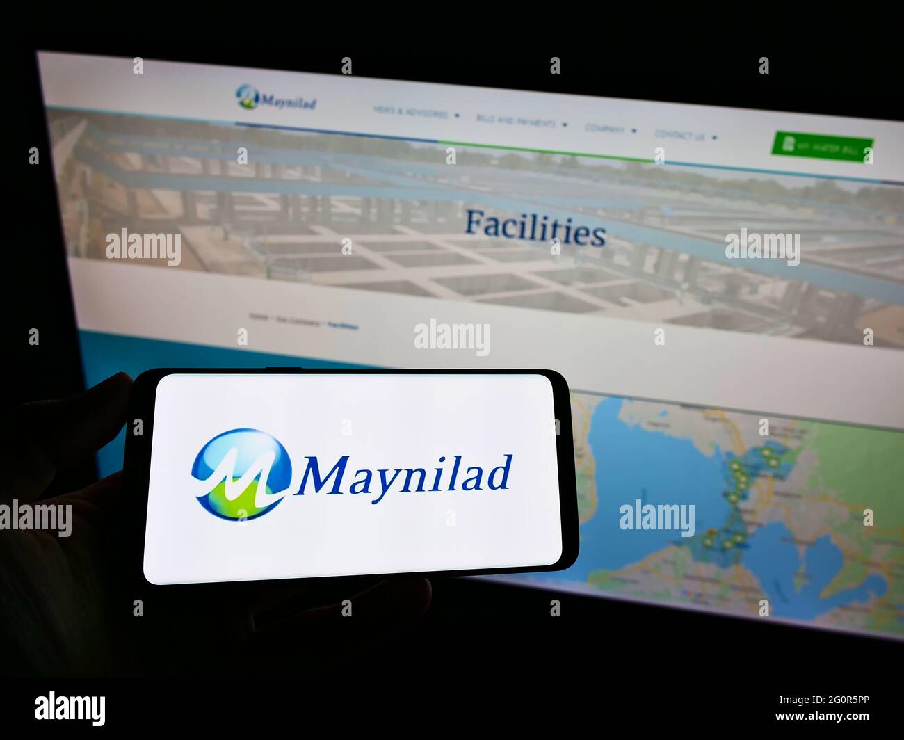 Person holding smartphone with logo of Philippine company Maynilad Water Services Inc. on screen in front of website. Focus on phone display. Stock Photo