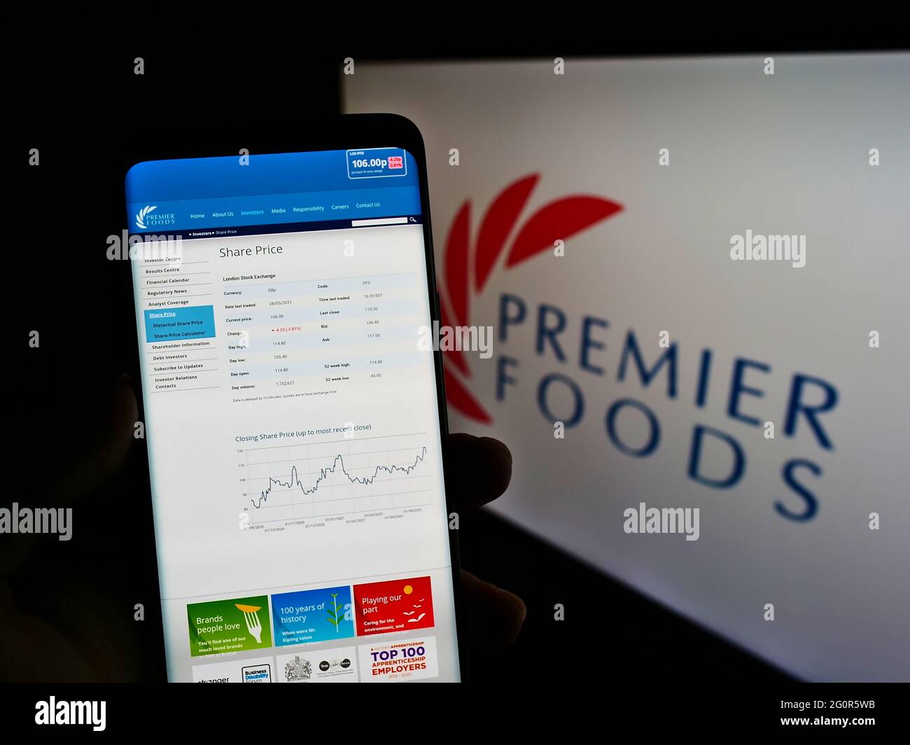 Person holding cellphone with website of British food manufacturer Premier Foods plc on screen in front of logo. Focus on center of phone display. Stock Photo