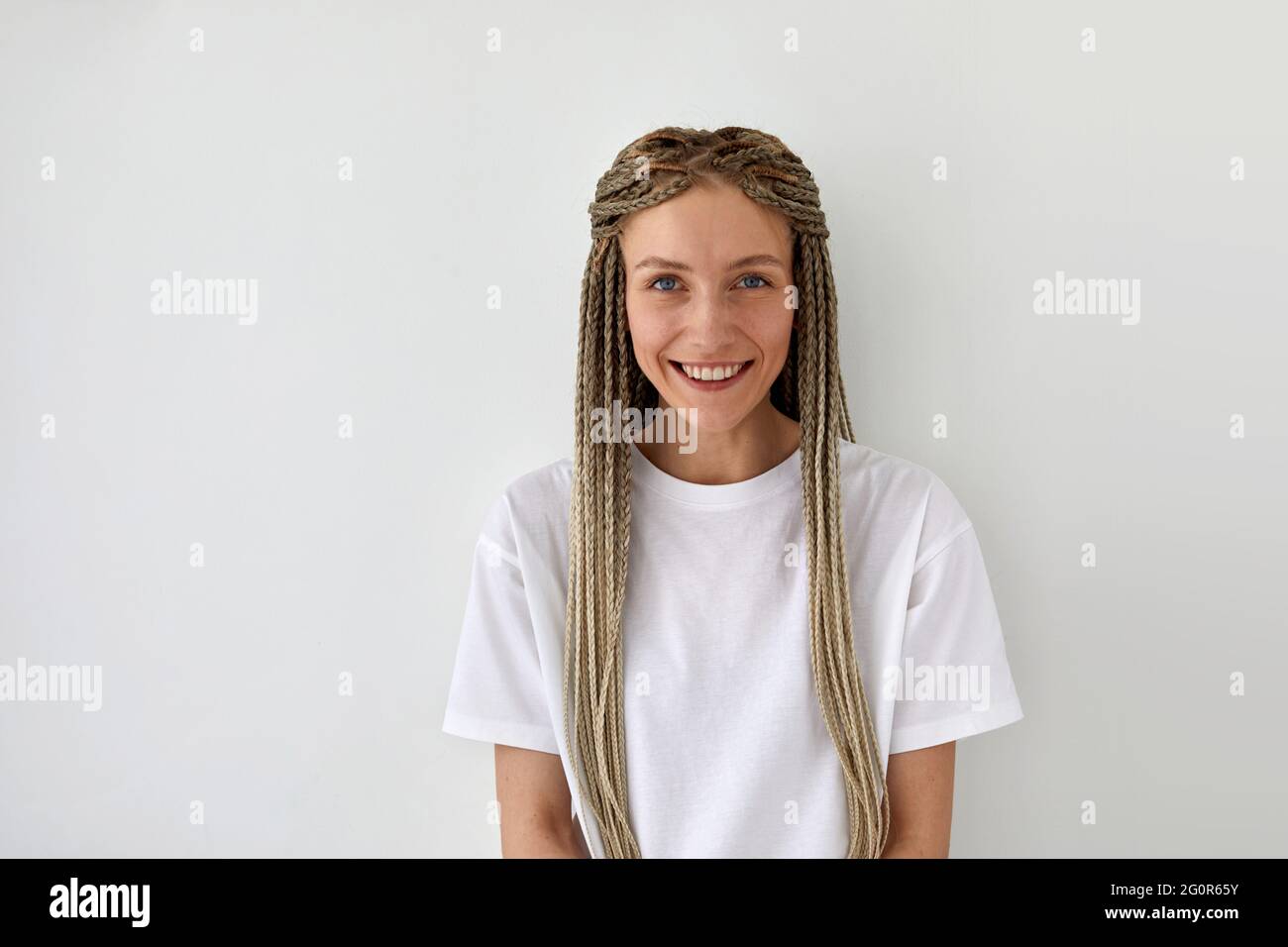 Cheerful attractive female with braids wearing casual white shirt standing on light background and looking at camera Stock Photo