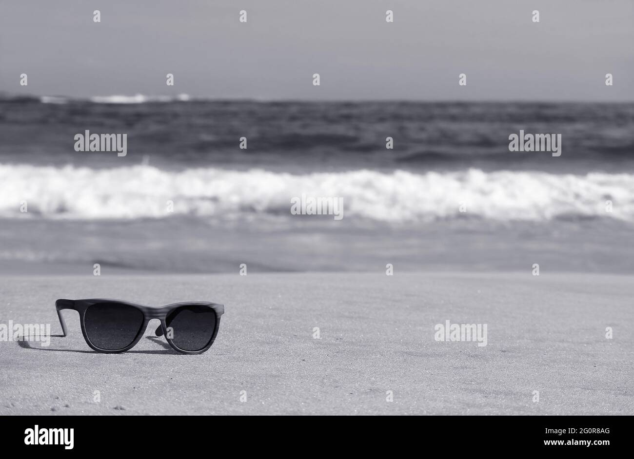 Monochrome image of a sunglasses on the beach with blurry splashing waves in background Stock Photo