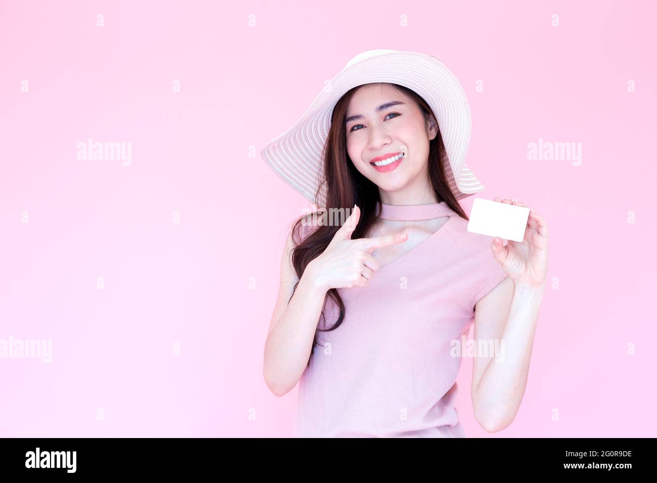 Beautiful young Asian woman smiling and presenting credit card with copy space pink background, Making payment for shopping online or flight ticket, E Stock Photo