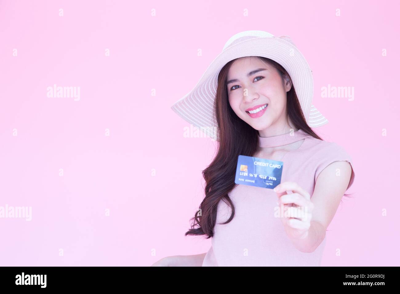 Beautiful young Asian woman smiling and presenting credit card with copy space pink background, Making payment for shopping online or flight ticket, E Stock Photo