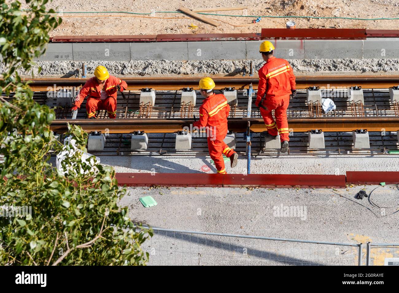 Tel Aviv, Israel - May 20 2021: Construction Workers with Orange overalls. Light rail tracks. blue collar worker. Concept Collaboration teamwork. Trucks, concrete mixer, bulldozer. High quality photo Stock Photo