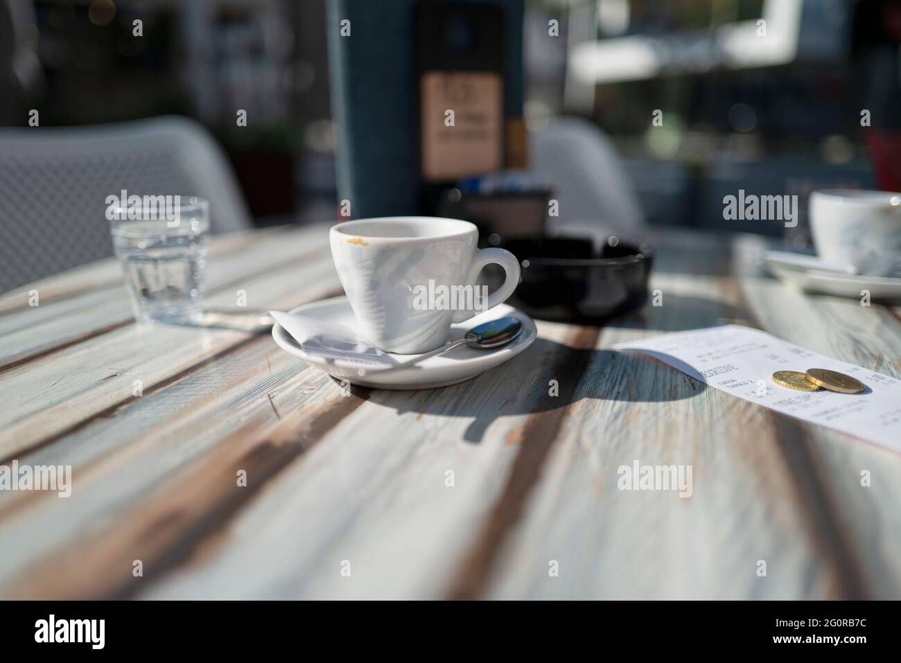 A small restaurant table at the sunny terrace after a short coffee break with the bill and some tip. Stock Photo