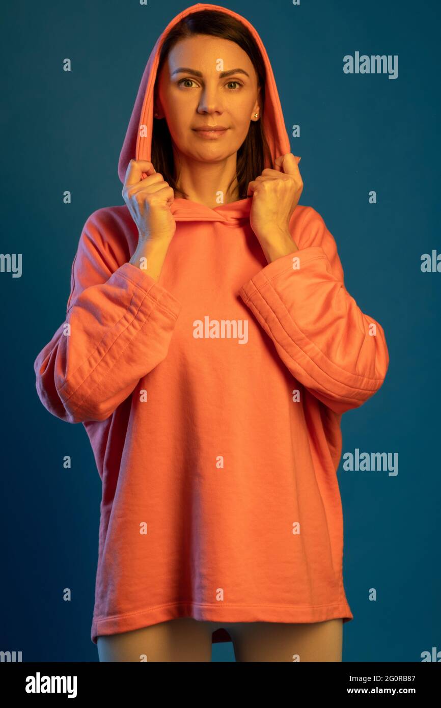 Smiling woman in hooded sweatshirt looking at camera against blue background Stock Photo