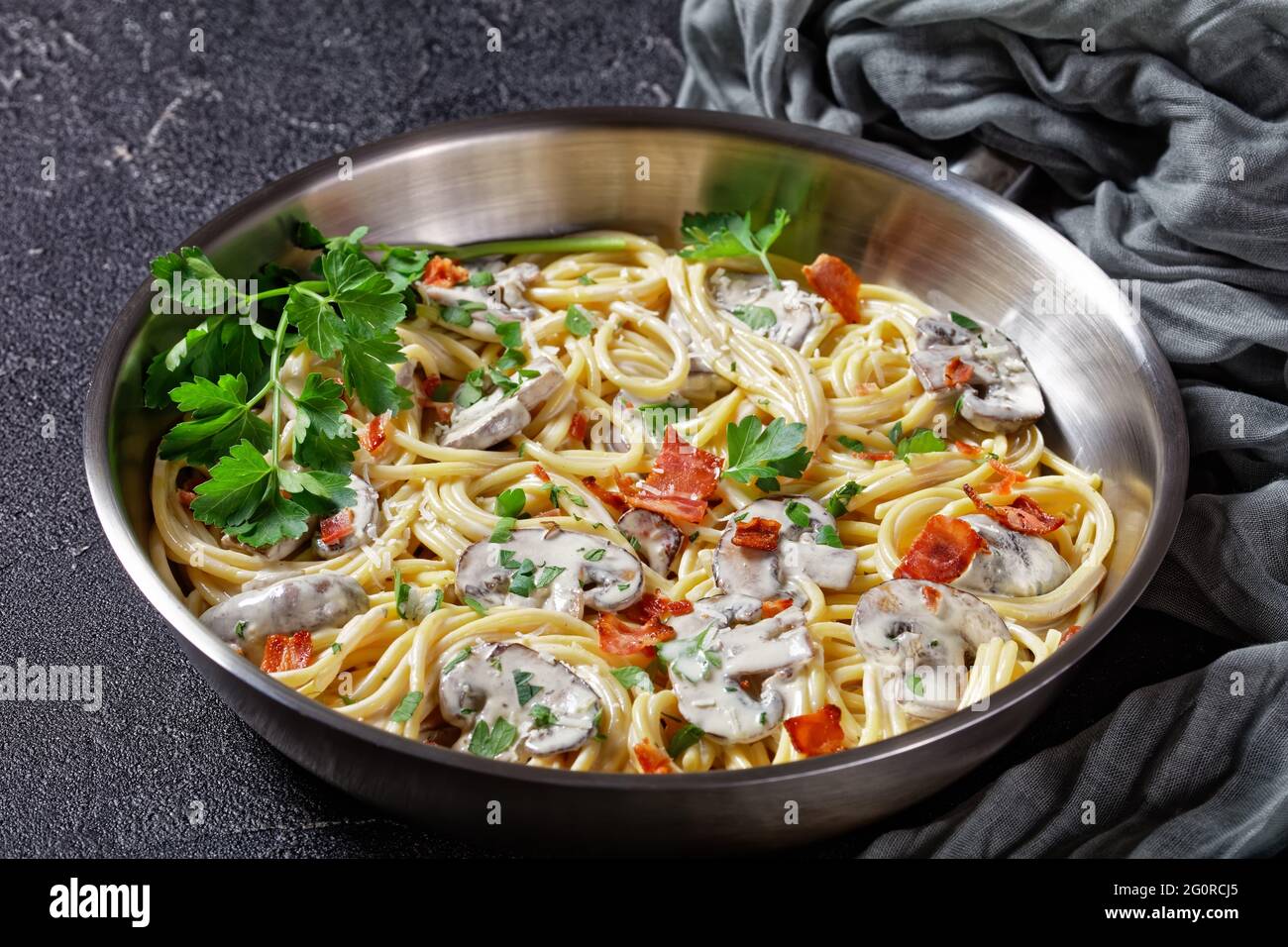 Italian pasta with cremini mushroom sauce of heavy cream and parmesan cheese with crispy bacon and fresh parsley served on a metal skillet on a dark Stock Photo