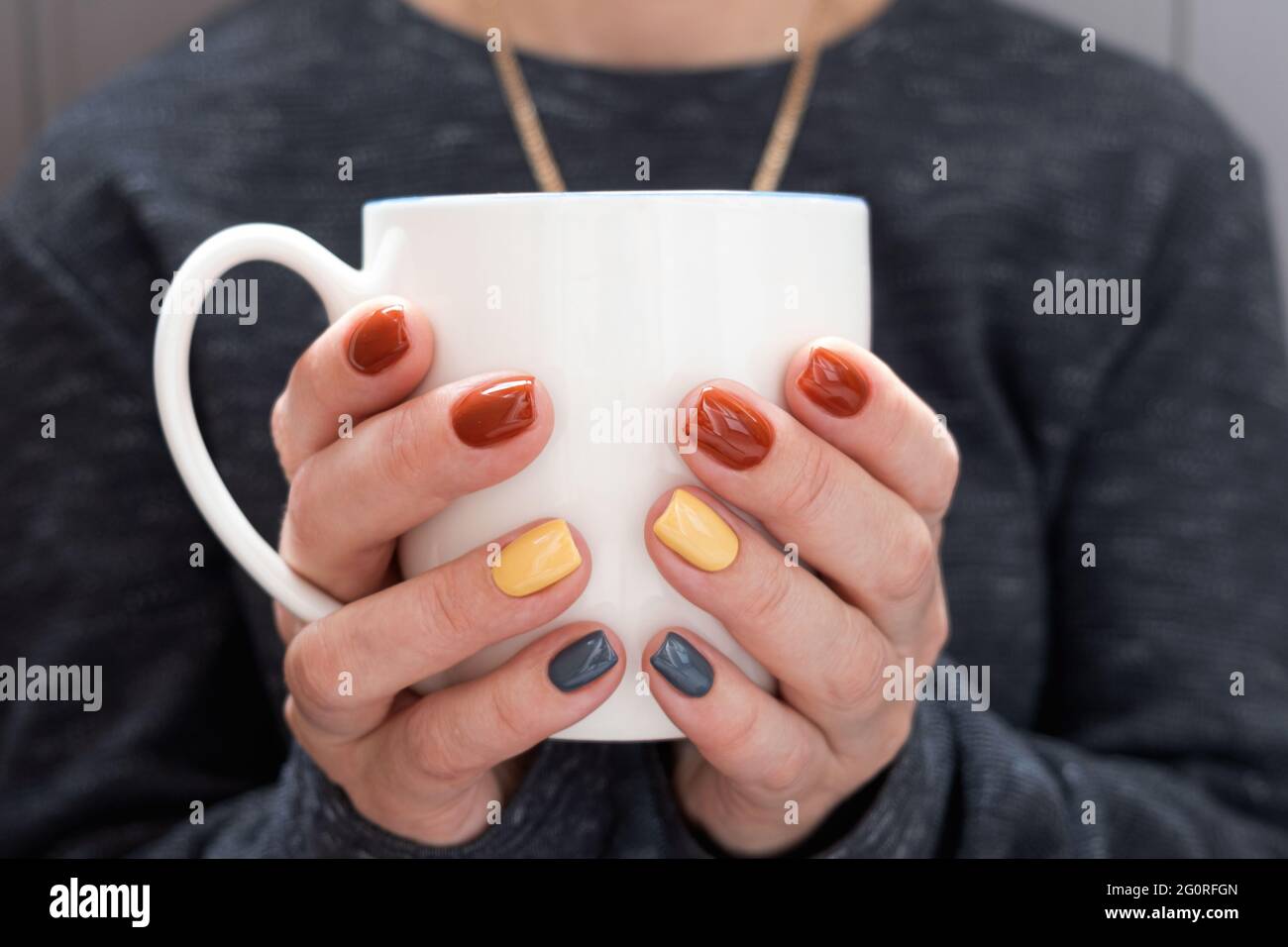 The girl warms up, holding a cup of coffee in her hands. Well-groomed hands beautiful manicure, design for any purpose. Blurred background Stock Photo