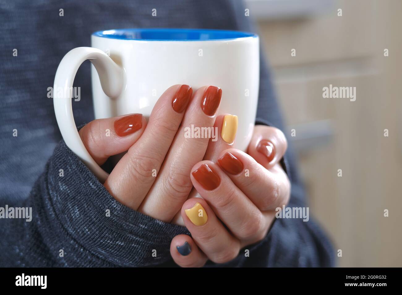 The girl warms up, holding a cup of coffee in her hands. Well-groomed hands beautiful manicure, design for any purpose. Blurred background Stock Photo