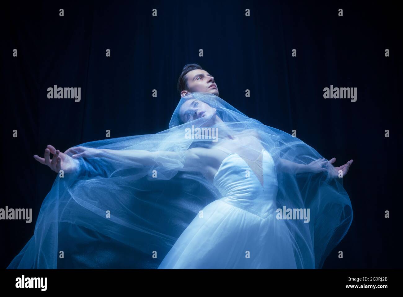 Young woman in wedding dress and man, two ballet dancers in art performance dancing isolated over dark background. Stock Photo