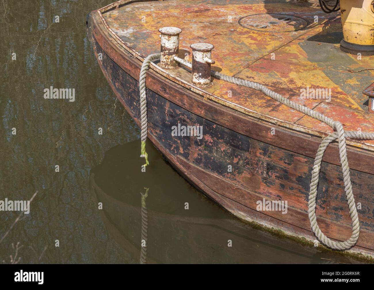 A rusting barge moored by rope with capstans and dark water. Stock Photo