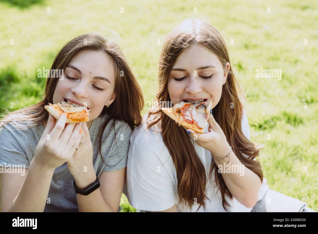 Two cheerful young teen friends in the park eating pizza. Women eat fast food. Not a healthy diet. Soft selective focus. Stock Photo
