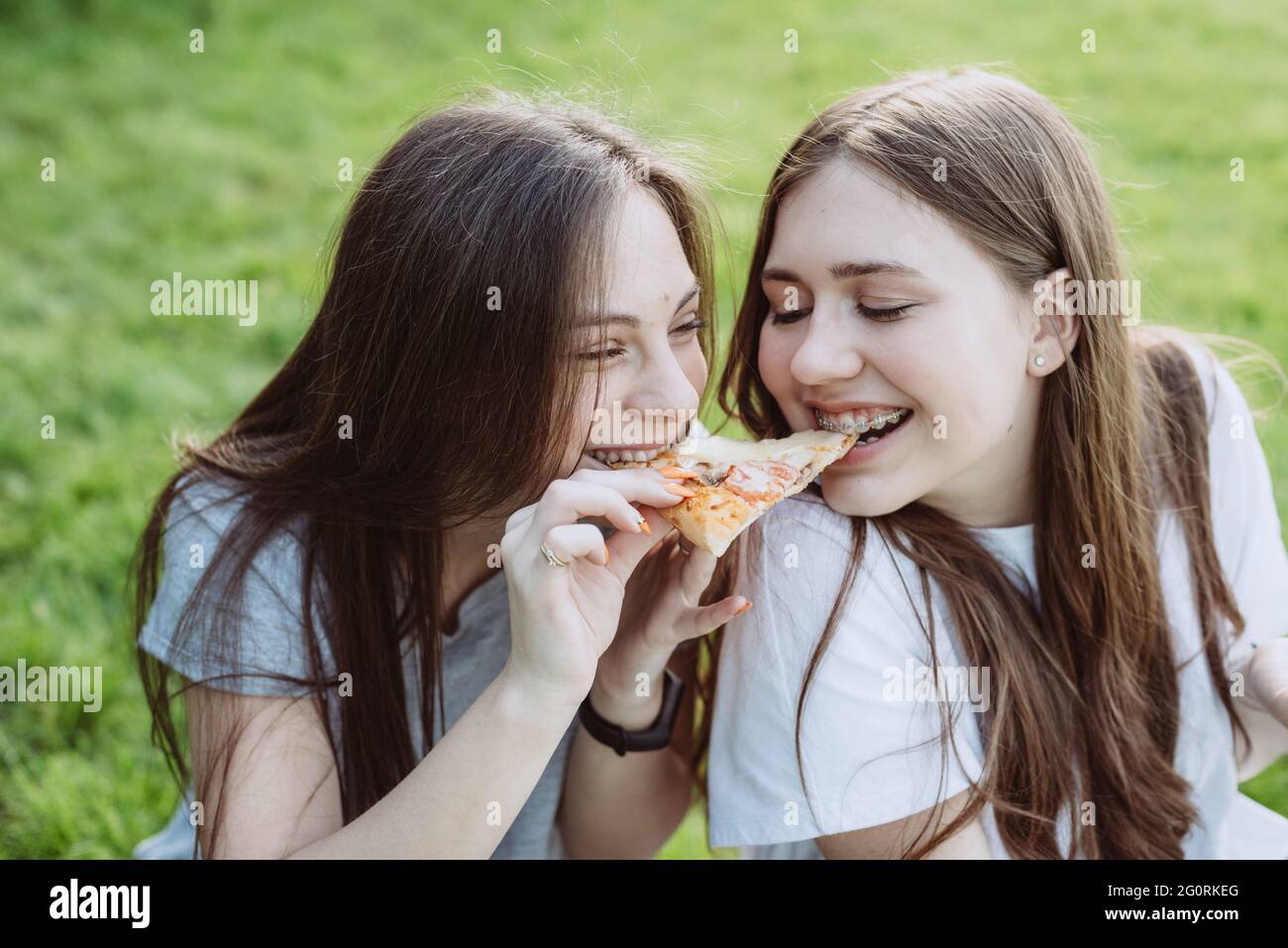 Two cheerful young teen friends in the park eating pizza. Women eat fast food. Not a healthy diet. Soft selective focus. Stock Photo