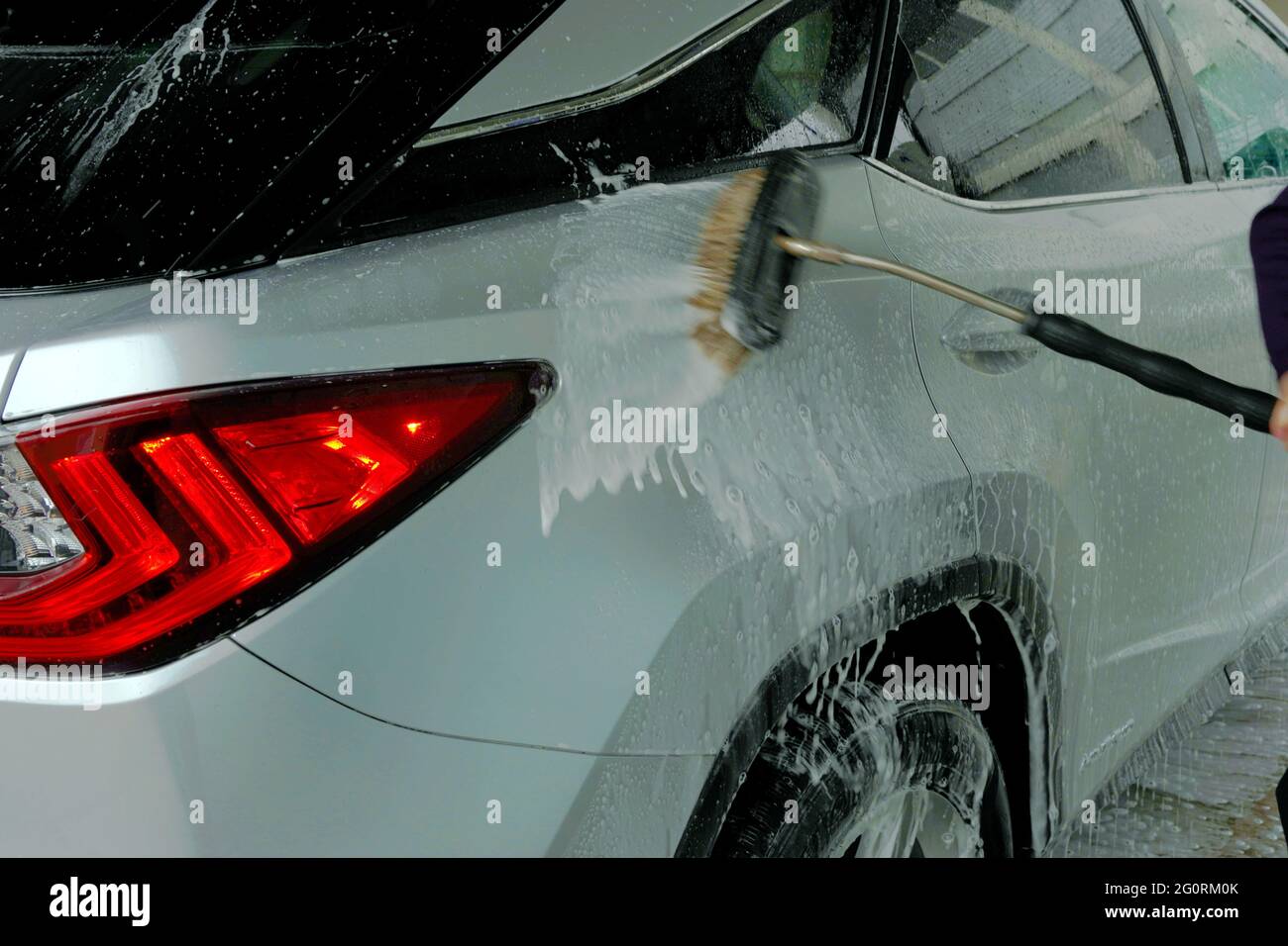 Man washing a car with a brush spreading shampoo over it. A scene from self service car wash
