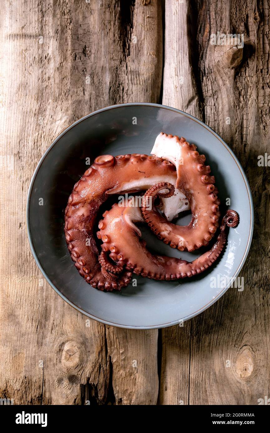 Coocked tentacles of octopus on blue ceramic plate over brown wooden background. Top view, flat lay Stock Photo