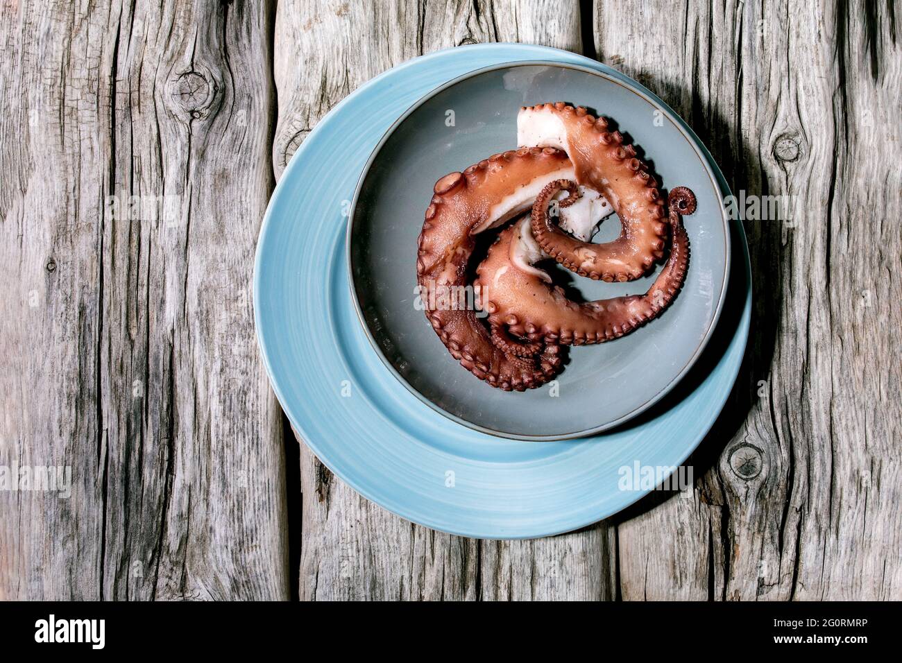 Coocked tentacles of octopus on blue ceramic plate over old grey wooden background. Top view, flat lay. Copy space Stock Photo
