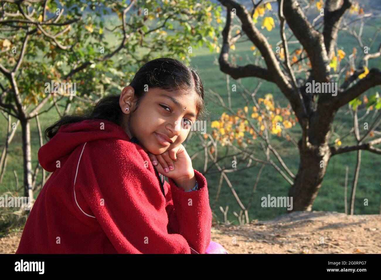 BENGALURU, INDIA - Jan 21, 2008: Indian girl in red sweater sitting in a park Stock Photo