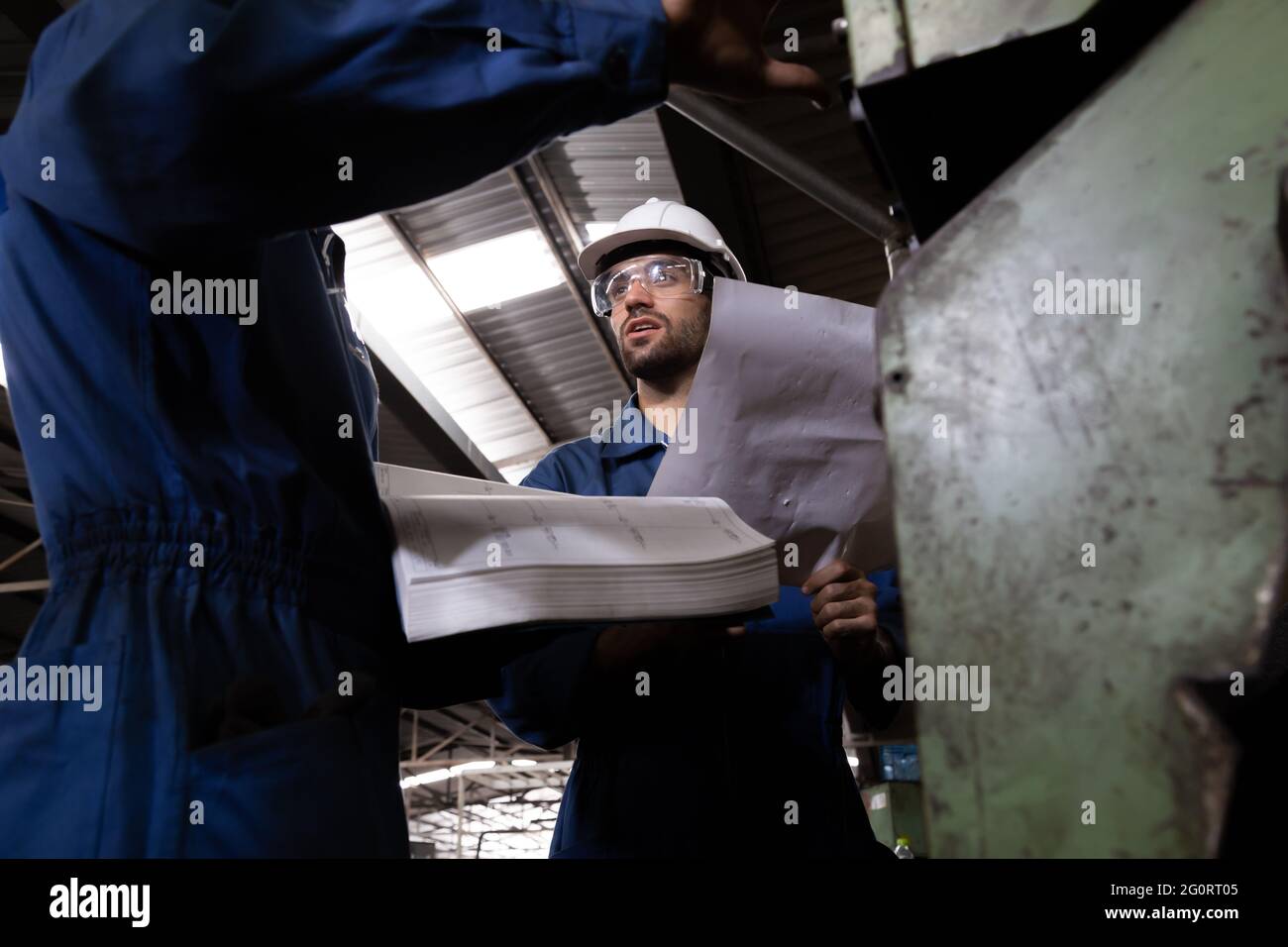 Factory engineer reading manual of machine operation and standing with blue working suite dress