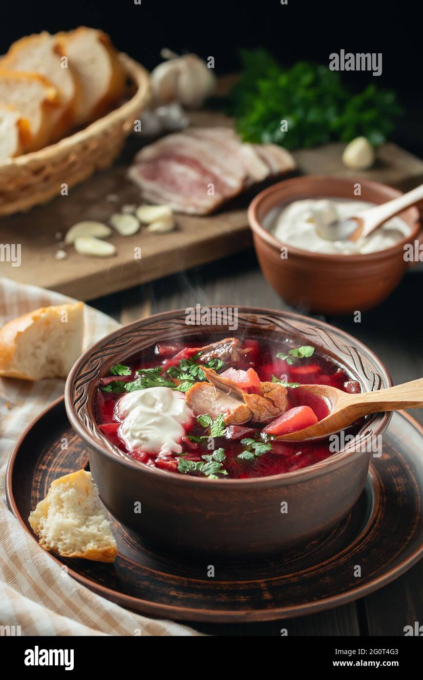 Freshly cooked borscht - traditional dish of Russian and Ukrainian cuisine in earthenware dishes with bacon, sour cream and garlic, vertical image. Stock Photo