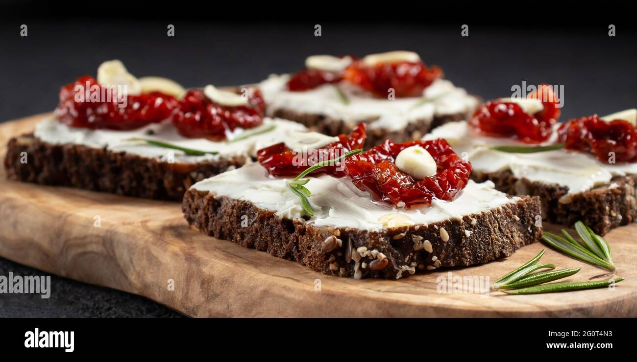 Homemade multigrain bread sandwiches with cream cheese and sun-dried tomatoes on a wooden platter. Healthy eating concept. Stock Photo