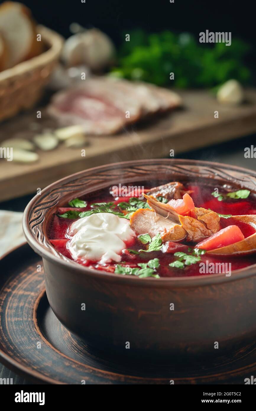 Freshly cooked borscht - traditional dish of Russian and Ukrainian cuisine in earthenware dishes with bacon, sour cream and garlic, vertical image. Stock Photo