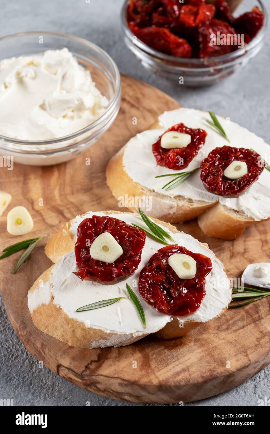 Homemade sandwiches with cream cheese and sun-dried tomatoes on a wooden board of olive - delicious healthy breakfast, italian cuisine, vertical image Stock Photo