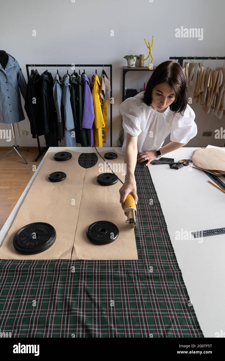 Dressmaker cut patterns of raincoat fabric with electric cutter in