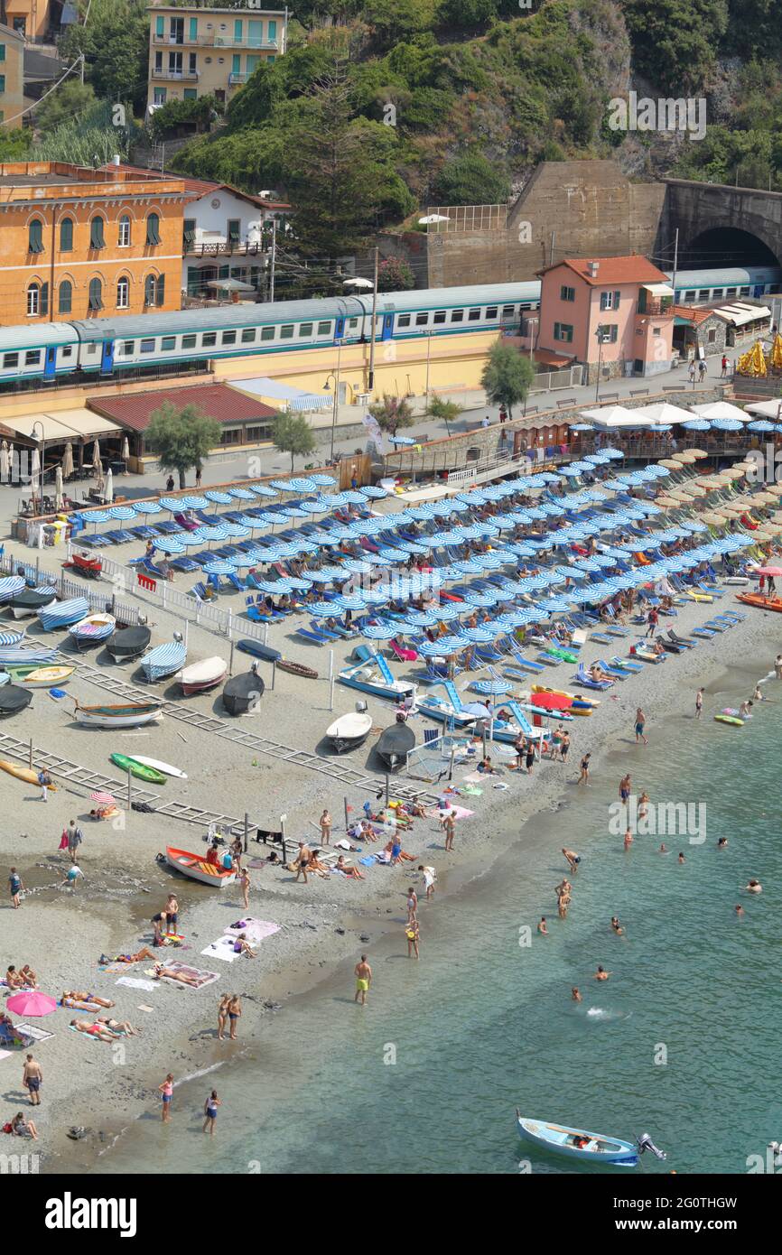 People resting on one of the beaches in Monterosso al Mare, the Cinque Terre national park, Italy, against Cinque Terre Express train entering tunnel Stock Photo