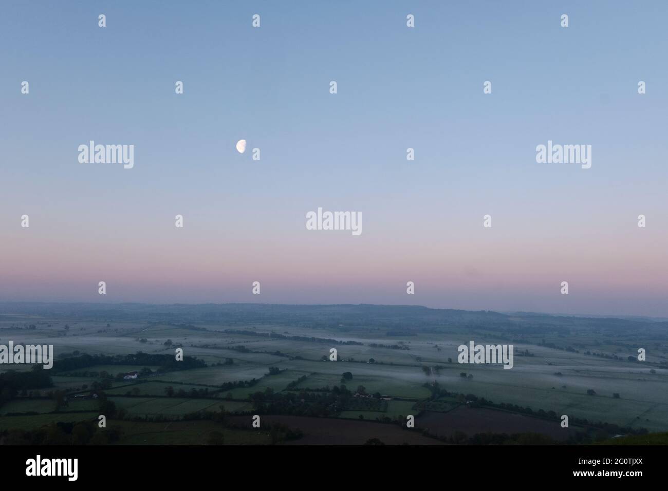Moon setting over the Somerset Levels at dawn in May, from Glastonbury Tor Stock Photo
