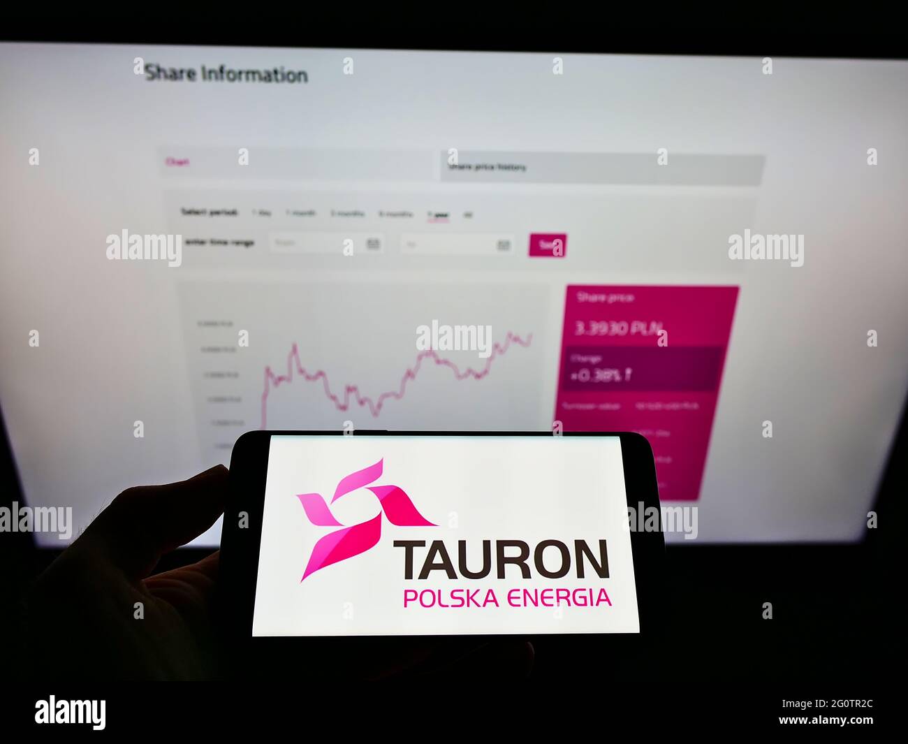 Person holding smartphone with logo of Polish energy company Tauron Polska Energia S.A. on screen in front of website. Focus on phone display. Stock Photo