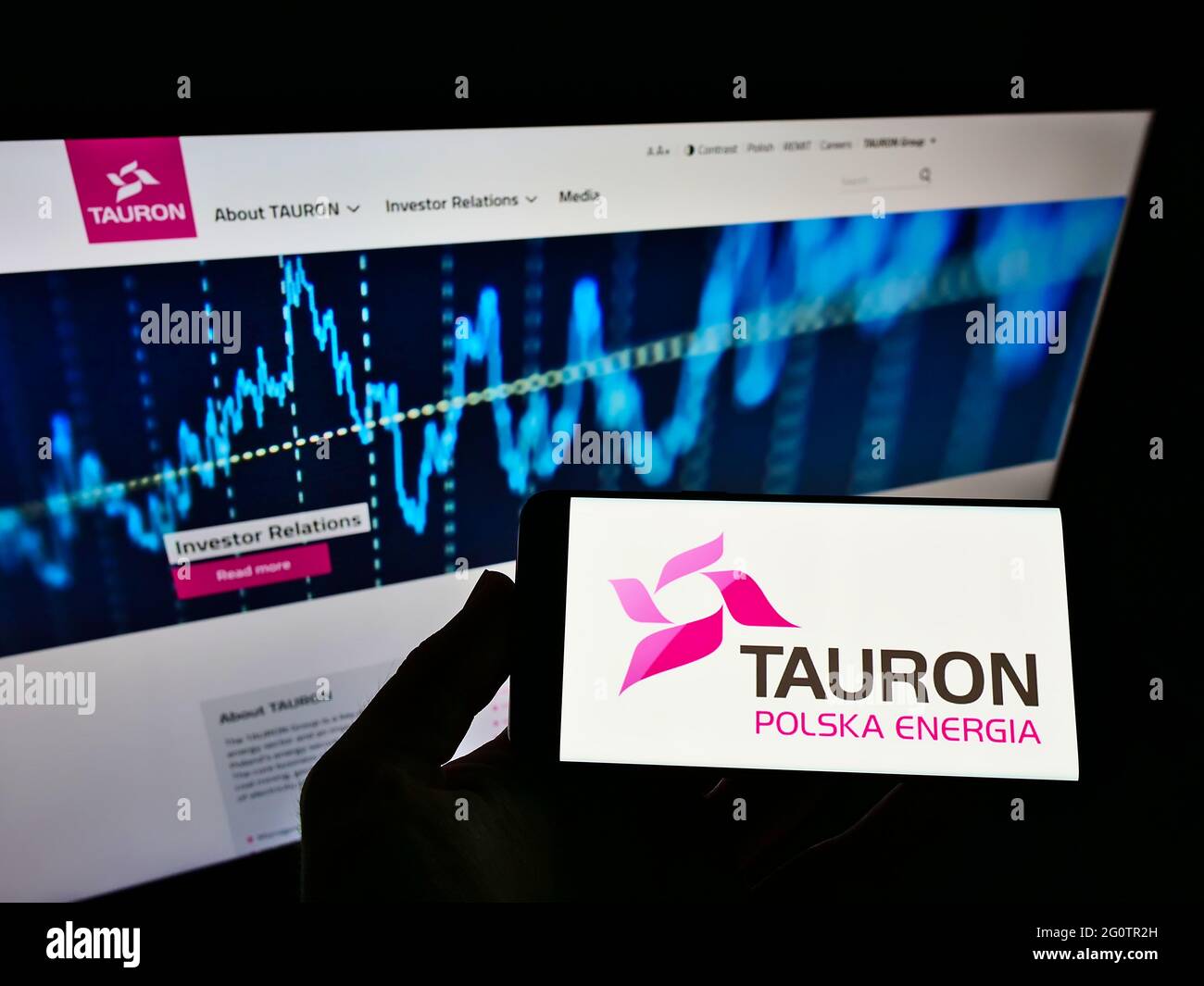 Person holding mobile phone with logo of Polish energy company Tauron Polska Energia SA on screen in front of web page. Focus on phone display. Stock Photo