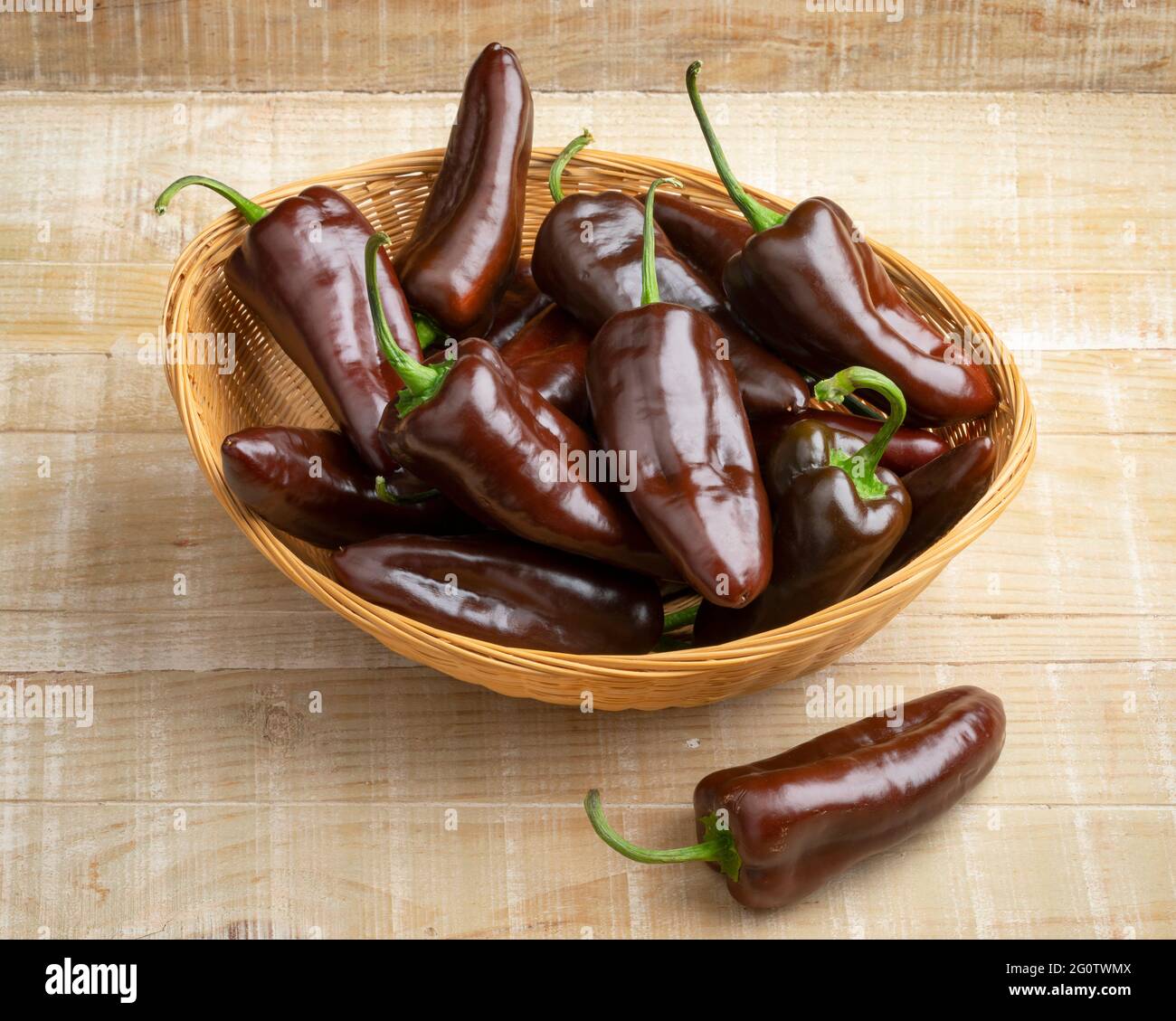 Basket with whole fresh chocolate mini pointed bell peppers close up on wooden background Stock Photo