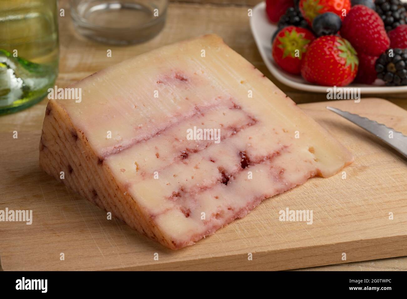 Piece of  Spanish goat cheese with red fruit syrup injected inside,  on a cutting board and fresh fruit in the background Stock Photo