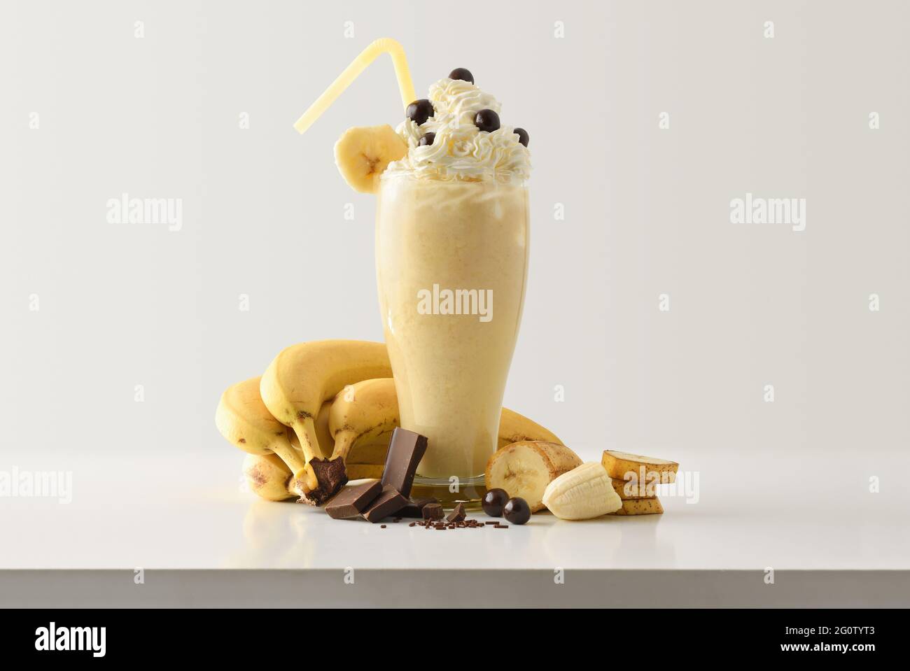 Banana milkshake with chocolate and cream decorated with fruit and chocolate portions around on white wooden table and light isolated background. Fron Stock Photo