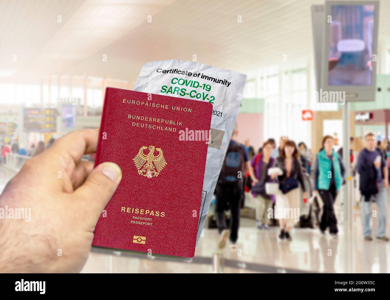 hand holding a Germany passport with a wrinkled paper Coronavirus Covid 19 immunity certificate. Blurred airport in the background. Immunity from Covi Stock Photo