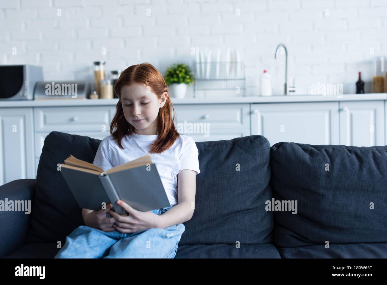 preteen girl reading book on sofa in kitchen Stock Photo - Alamy