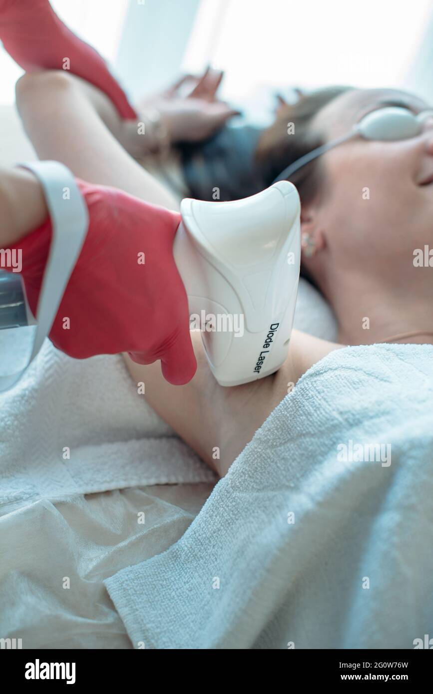 A woman beautician makes a diode laser epilation procedure. Laser hair removal of armpits with the help of a diode laser Stock Photo