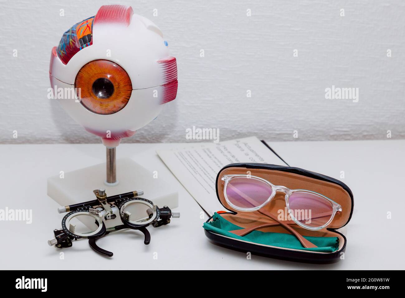 On a table there is a model of an eye, some glasses to graduate the vision, some new glasses in their case and a reading letter Stock Photo