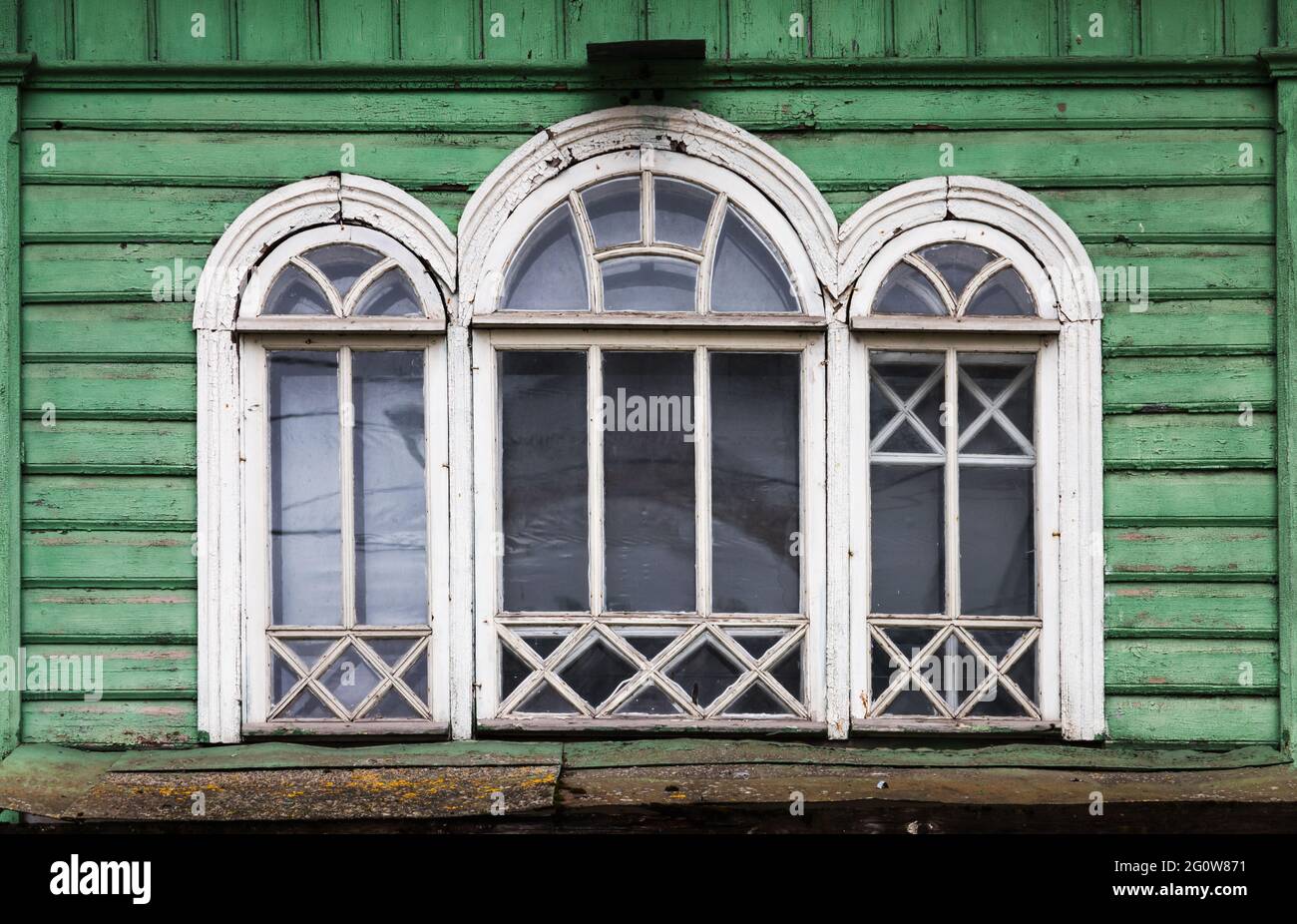 Triple arched window with white wooden frame in grungy green wooden wall, Russian rural architecture background photo fragment Stock Photo