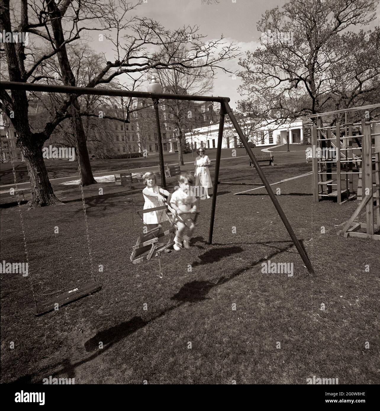 ST-C66-14-63                                                       1 April 1963  Caroline Kennedy and John F. Kennedy, Jr. playing on a swingset. South Lawn, White House, Washington, D.C.  Please credit 'Cecil Stoughton. White House Photographs. John F. Kennedy Presidential Library and Museum, Boston' Stock Photo