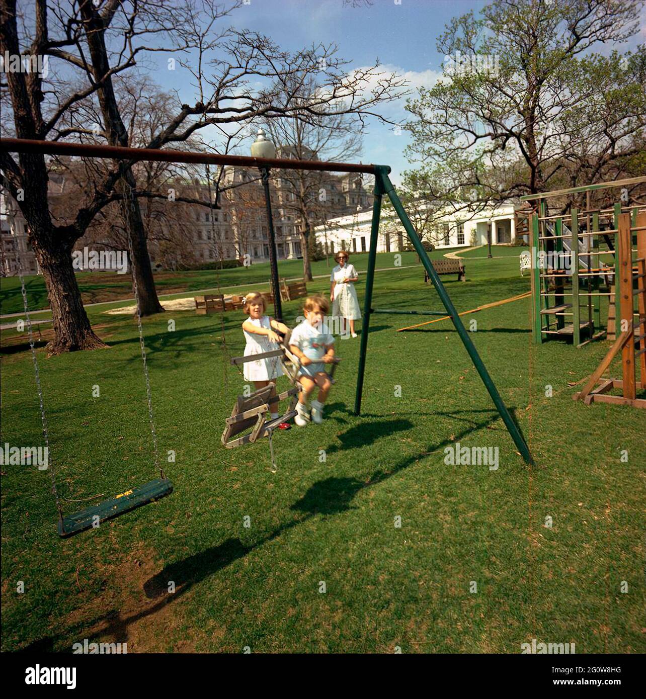 ST-C66-14-63                                                       1 April 1963  Caroline Kennedy and John F. Kennedy, Jr. playing on a swingset. South Lawn, White House, Washington, D.C.  Please credit 'Cecil Stoughton. White House Photographs. John F. Kennedy Presidential Library and Museum, Boston' Stock Photo
