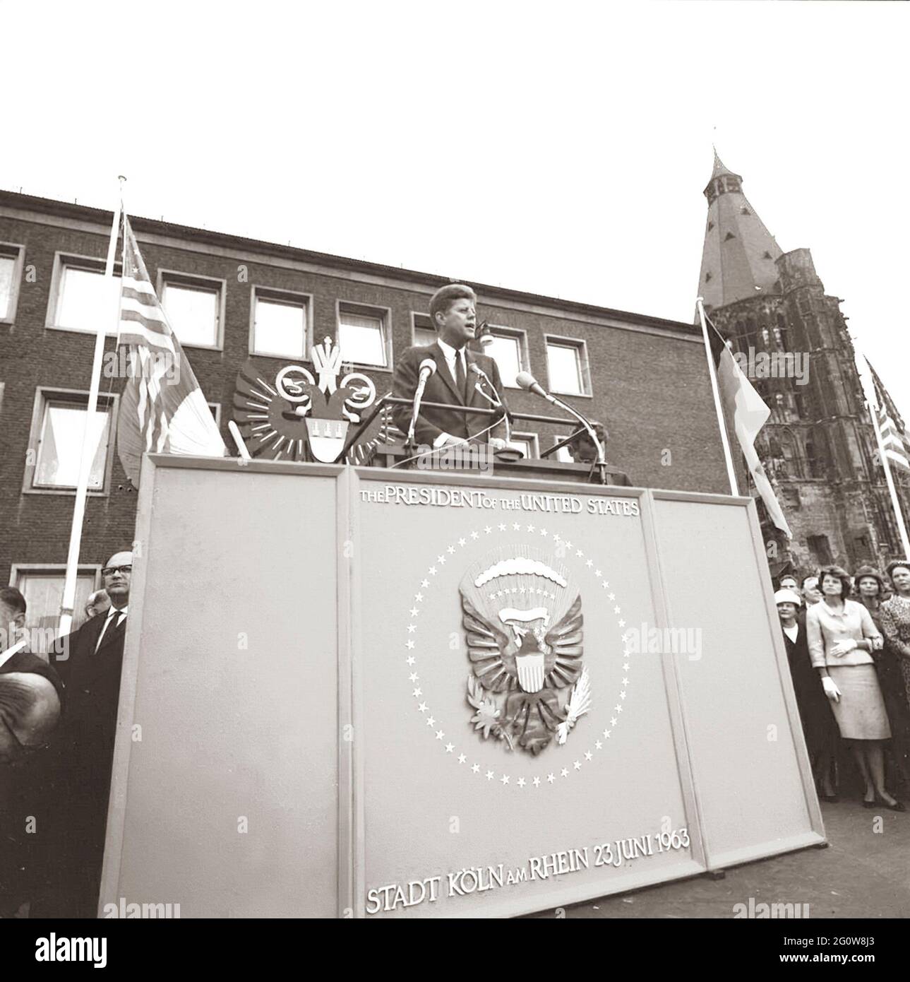 KN-C29238                              23 June 1963  President John F. Kennedy's visit to Cologne. President Kennedy stands at a speakers podium with interpreter Robert H. Lochner at his side. Eunice Shriver and others view the President's address. City Hall, Cologne, Germany.  Please credit 'Robert Knudsen. White House Photographs. John F. Kennedy Presidential Library and Museum, Boston' Stock Photo