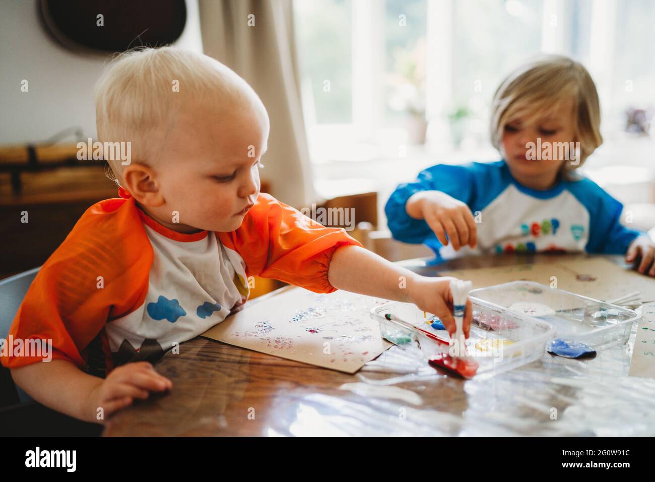 Blonde young children painting with lots of colorful paints at home Stock Photo