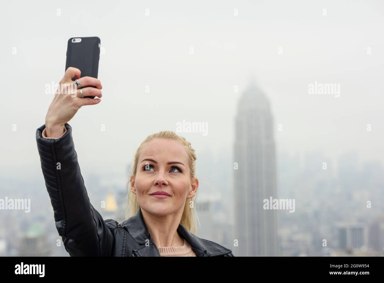 Cheerful woman taking selfie against modern skyscraper in foggy metropolis Stock Photo