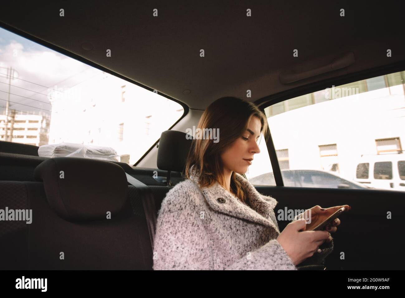 Non-binary woman using smart phone while traveling in car Stock Photo